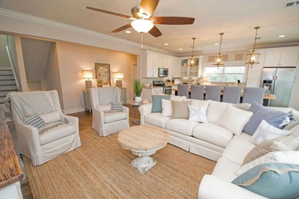 Open-concept living room with cream sectional, two armchairs, a round wooden coffee table, and a white-kitchen island in the background.